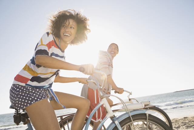 A young woman and man biking by the beach in the sun